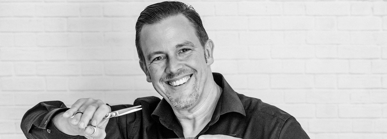 André Schilling, Inhaber und Friseurmeister, lachend mit einer Schere in der Hand