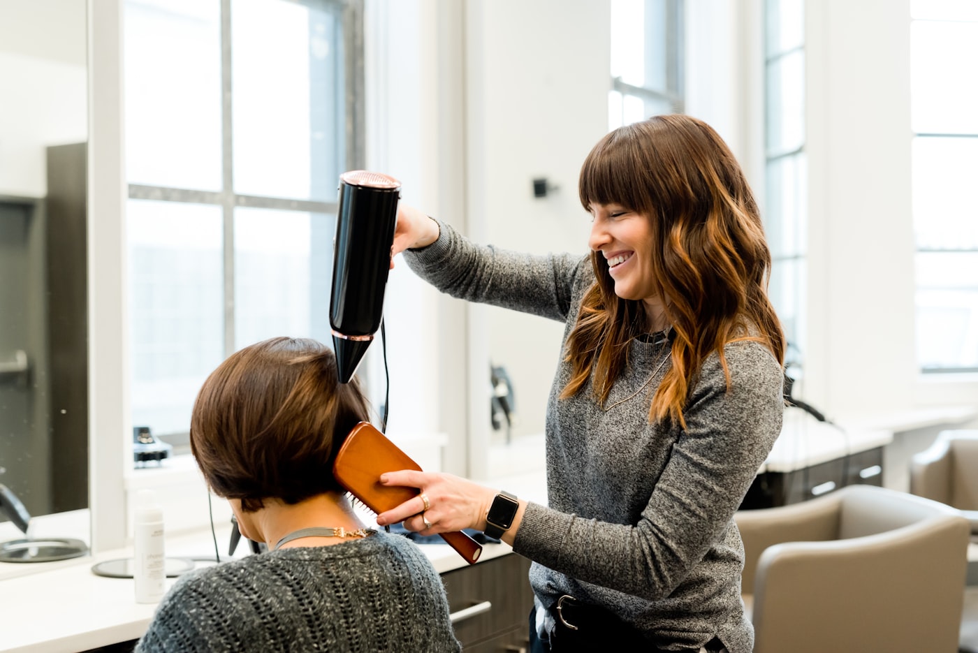 Stylistin föhnt lachend die Haare einer Kundin