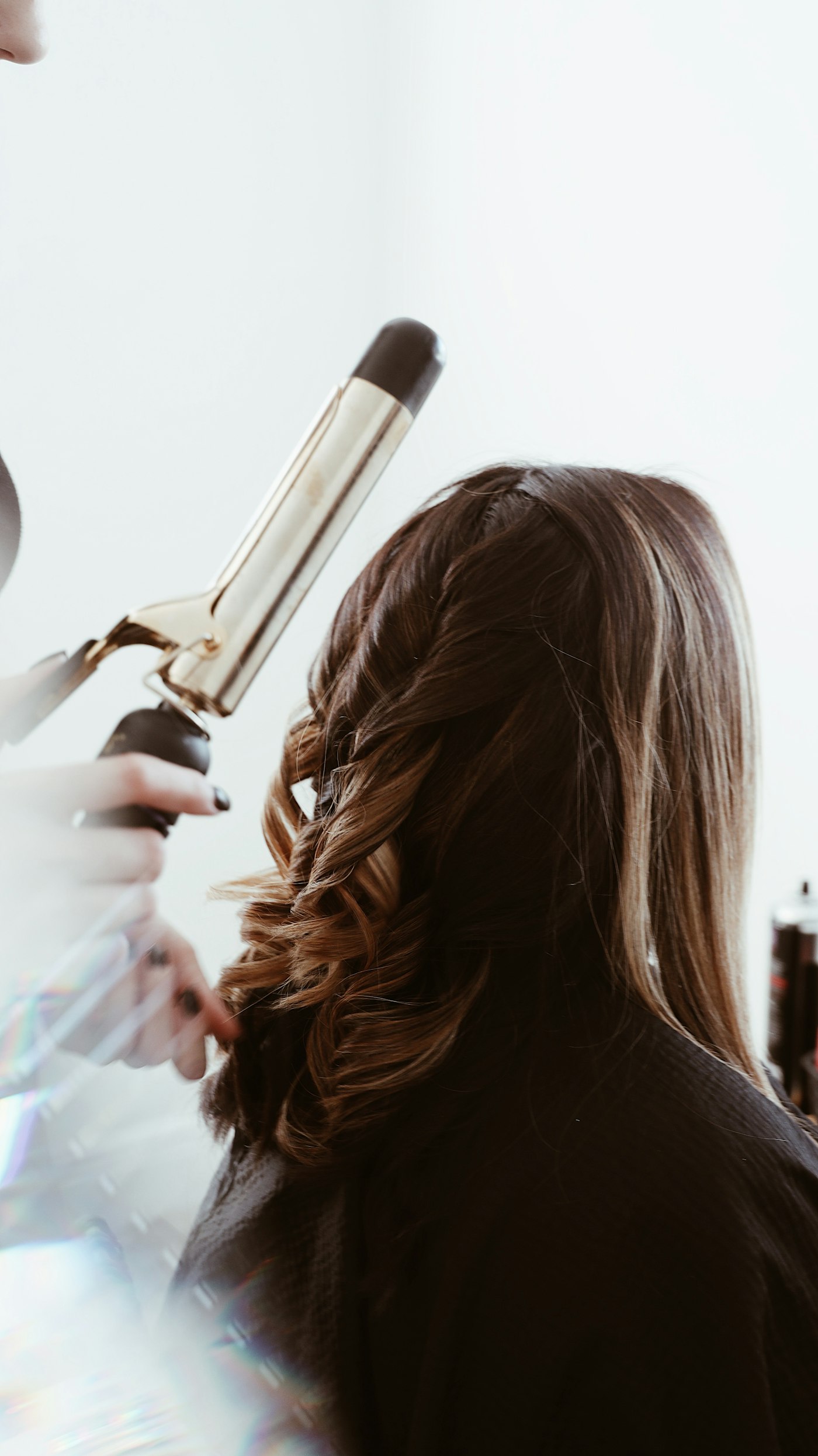 Haare werden mit einem Lockenstab in Form gebracht